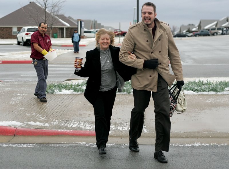 Custodian Jose Perez continues to salt the walk way as Will Bryant, a fourth grade intern at Bayyari Elementary School in Springdale, escorts Meredith Cox, instructional facilitator, across the patches of ice covering parts of the sidewalk and entry in front of the school Thursday morning. Freezing rain and sleet continued through the morning with the National Weather Service in Tulsa predicting up to half an inch of ice accumulations possible. 