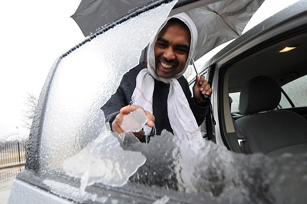 Shihab Kavungathodika pokes away at a sheet of ice Thursday that remained after rolling the window down on his roomate’s vehicle outside his apartment in Bentonville. Kavungathodika and his roommates were working on de-icing the car before heading to work. Northwest Arkansas was spared the brunt of a winter storm initially forecasted to dump up to a half inch of ice across the area. 