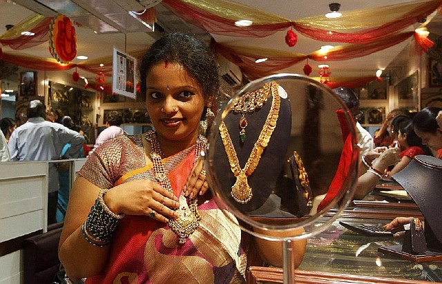 In this Thursday, Feb. 14, 2013 photo, an Indian woman looks into a mirror as she tries out gold jewelry at a shop in Mumbai, India. Nowadays, India is by far the world's biggest buyer of gold, which despite its rising value, is an increasing drain on an economy that is growing too slowly to reduce widespread poverty. Last year Indians imported 864 tons of gold, about one fifth of world sales. The cost of 2.5 trillion rupees ($45 billion) was second only to India's bill for oil imports. The unquenchable appetite for gold coins, bars and jewelry has swelled India's trade deficit and weakened its currency, making crucial imports such as fuel more expensive. (AP Photo/Rajanish Kakade)
