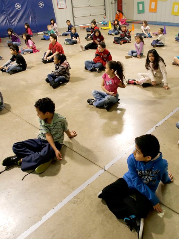 Second-graders in Josh Hicklin’s physical education class stretch Monday morning in the gym at Elmdale Elementary School in Springdale. The school has received a $10,000 grant from Lowe’s to install a new floor and padding in its gym to make it safer for the kids. 