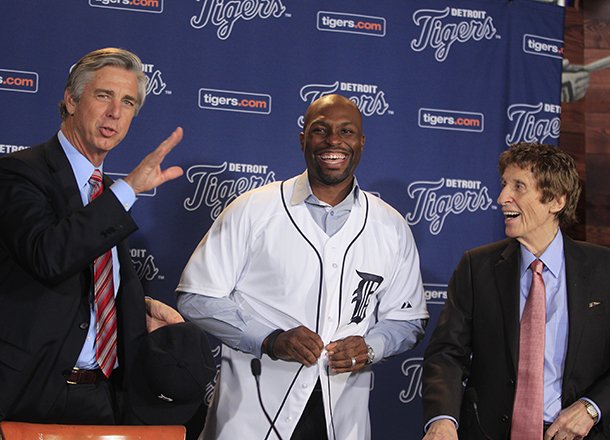 Detroit Tigers outfielder Torii Hunter, smiles after putting on his jersey as team general manager David Dombrowski, left, and owner Mike Ilitch look on before a news conference in Detroit, Friday, Nov. 16, 2012. Hunter, who last played for the Los Angeles Angels, signed a two-year, $26 million deal. (AP Photo/Carlos Osorio)
