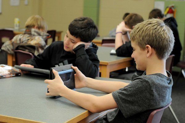 McNair Middle School sixth-grade students Nick Pilkington, right, 12, and Max Olsen, 12, read Wednesday on their electronic readers in the BYOD (Bring Your Own Device) program at the school in Fayetteville. The program allows students to use iPhones, iPads, Nooks and other electronic reading devices to read books or do approved research at the school. 