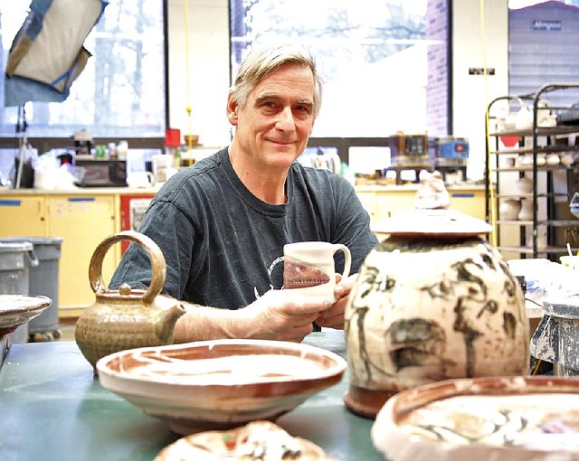 Potter Stephen Driver sits with pots by acclaimed potter Ron Meyers (foreground) and his own, the mug he holds and a teapot at left. Driver, assistant professor of art at the University of Arkansas at Little Rock, has co-curated a show for Meyers, his teacher, at the Arkansas Arts Center. 