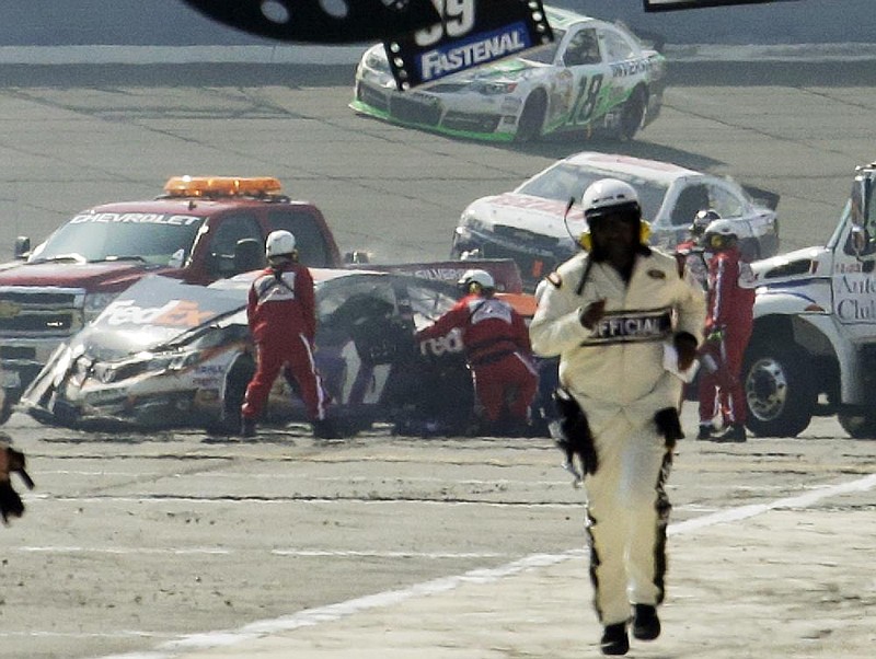 Rescue workers attend to the damage of Denny Hamlin’s car (left) after he collided with Joey Logano in the Auto Club 400 on Sunday afternoon in Fontana, Calif. 