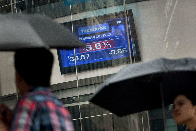 Pedestrians pass a monitor displaying Facebook’s share price at the Nasdaq MarketSite in New York on May 21, 2012. Nasdaq OMX Group Inc. will pay $62 million to compensate brokers for its mishandling of Facebook Inc.’s initial public offering on May 18, 2012. 