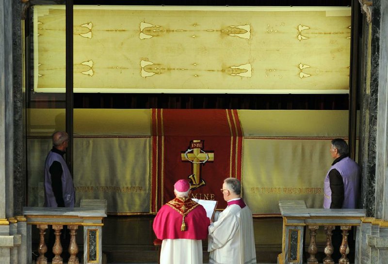 Archbishop of Turin Cesare Nosiglia, second left, watches the Shroud of Turin, on display for a special TV appearance Saturday, March 30, 2013. The Shroud went on display amid new research disputing claims it's a medieval fake and purporting to date the linen some say was Jesus' burial cloth to around the time of his death. Pope Francis sent a special video message to the event in Turin's cathedral, but made no claim that the image on the shroud of a man with wounds similar to those suffered by Christ was really that of Jesus. He called the cloth an "icon," not a relic  an important distinction. "This image, impressed upon the cloth, speaks to our heart and moves us to climb the hill of Calvary, to look upon the wood of the Cross, and to immerse ourselves in the eloquent silence of love," he said. (AP Photo/Alessandro Di Marco, Pool)