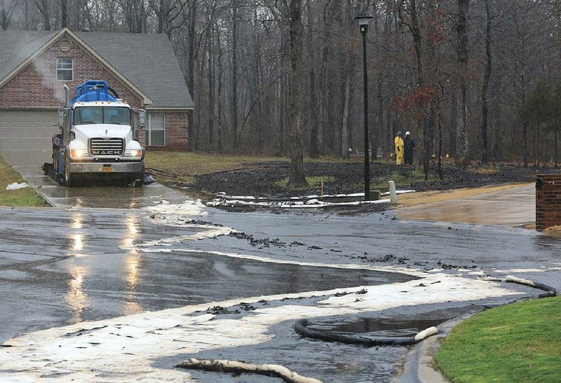 A cleanup truck sits in a driveway near spilled oil and boom material Saturday in Mayflower as workers in protective clothing confer near the site of an underground crude-oil pipeline break. 