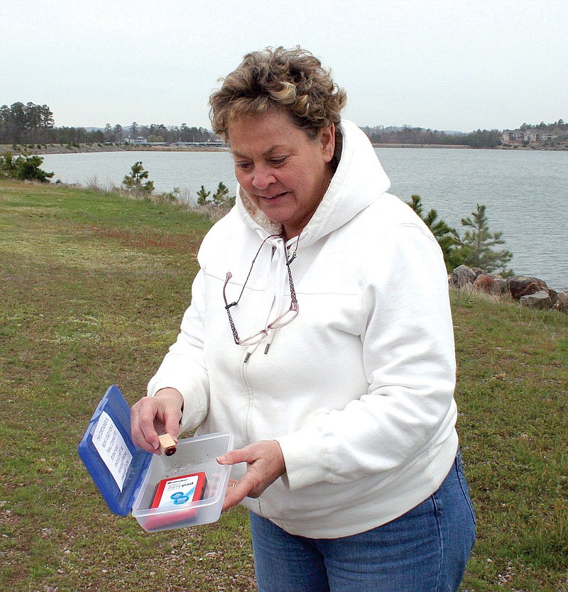 Valerie Derryberry, a member of the Hot Springs Village Trails Committee, takes a rubber stamp from a letterbox placed along a lakeside trail. The stamp is one of nine that residents are asked to find during April. Participants will record the stamps on a contest form. Those who collect all nine will be invited to a picnic in May.