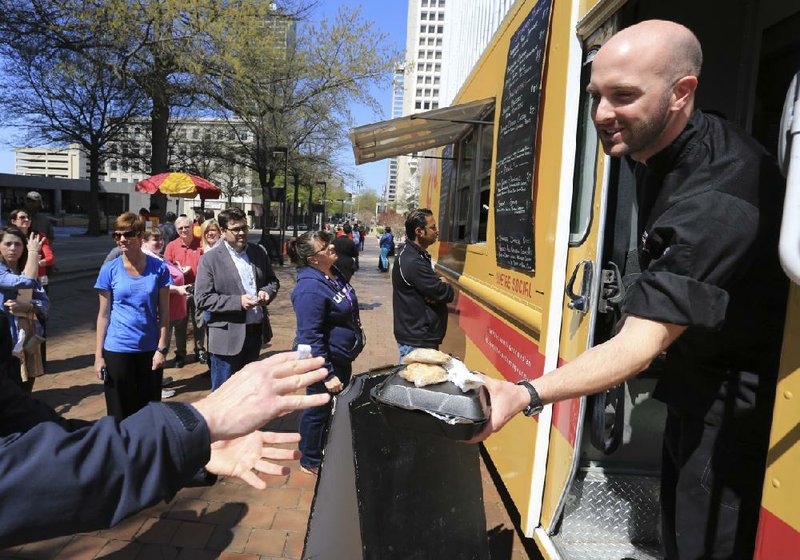 Justin Patterson hands out finished orders from the Southern Gourmasian truck to patrons visiting the Main Street Food Truck Fridays in Little Rock in this April 5, 2013, photo.