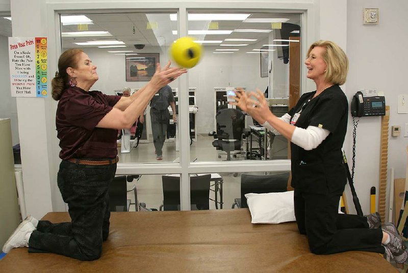 Martha White (left) and M.J. Orellano, program manager for outpatient therapy at the University of Arkansas for Medical Sciences, work on their core endurance and stability by tossing a weighted ball back and forth. 