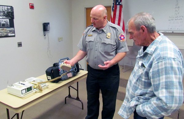 Dean Bitner, left, captain with the Springdale Fire Department, shows Lawrence “Ray” Bartlett two Life Pack machines Thursday at Station No. 1 in Springdale. The machine on the left, or one the same model, was used by firefighters to start Bartlett’s heart in 1993. Bitner was a member of the team that responded to that call. Bartlett hadn’t seen any of the team since his heart attack until this year. 