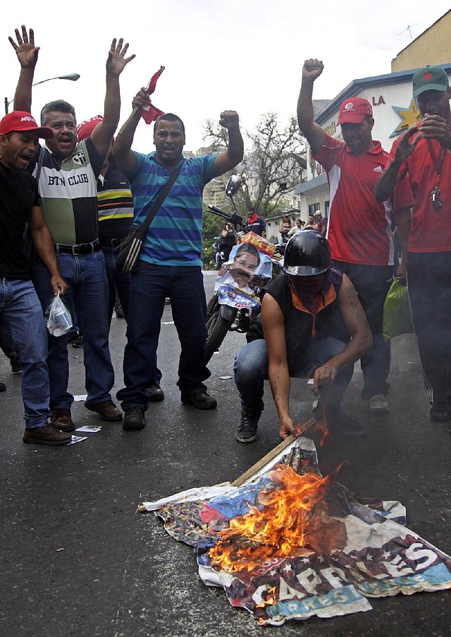 Government "Chavista" supporters burn an election poster of opposition presidential candidate Henrique Capriles in Los Teques, on the outskirts of Caracas, Venezuela, Tuesday, April 16, 2013.  President-elect Nicolas Maduro is blaming Capriles for seven deaths that the government says occurred in post-election unrest. The government has provided names of some people it says have been killed by opposition activists but has provided no evidence. Capriles is demanding a vote-by-vote recount of Sunday's presidential election. (AP Photo/Ariana Cubillos)