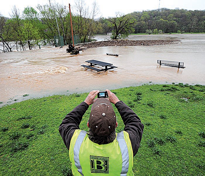 Robert Brown of the Bentonville Parks and Recreation Department snaps a photo Thursday of floodwaters overrunning the dam at Lake Bella Vista Park.