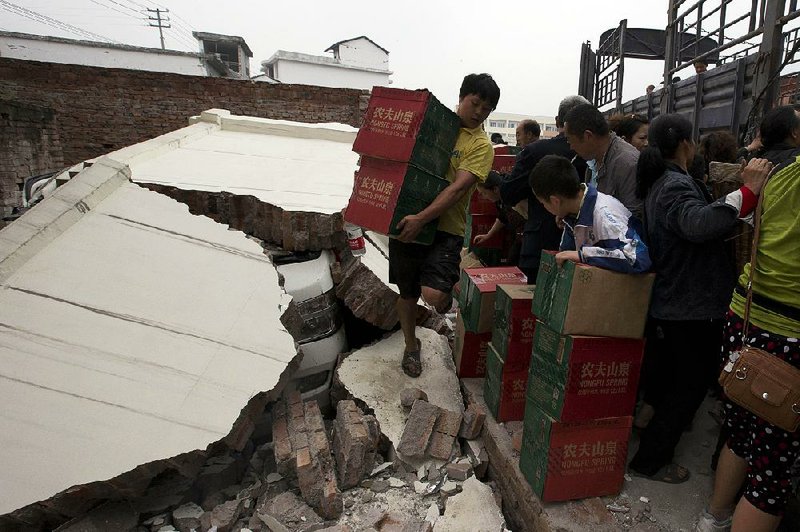 A man carrying boxes of water walks on the remains of a wall that had collapsed onto a vehicle after an earthquake struck the county seat of Lushan in southwestern China's Sichuan province, Monday, April 22, 2013. Saturday's earthquake in Sichuan province killed at least 186 people, injured more than 11,000 and left nearly two dozen missing, mostly in the rural communities around Ya'an city, along the same seismic fault where a devastating quake to the north killed more than 90,000 people in Sichuan and neighboring areas five years ago in one of China's worst natural disasters. (AP Photo/Ng Han Guan)