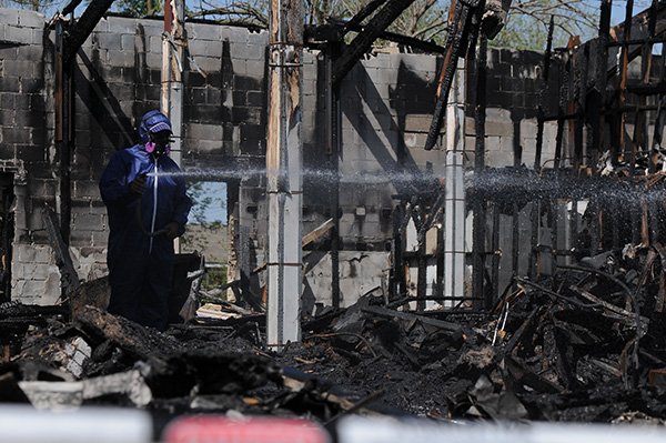 worker with Snyder Environmental of North Little Rock sprays debris with water Thursday, April 25, 2013 to keep dust to a minimum while others remove the charred remains of a former church on Grove Avenue and Thompson Street in Springdale. The church burned in January, but a threat of asbestos contamination was keeping the building from demolition.