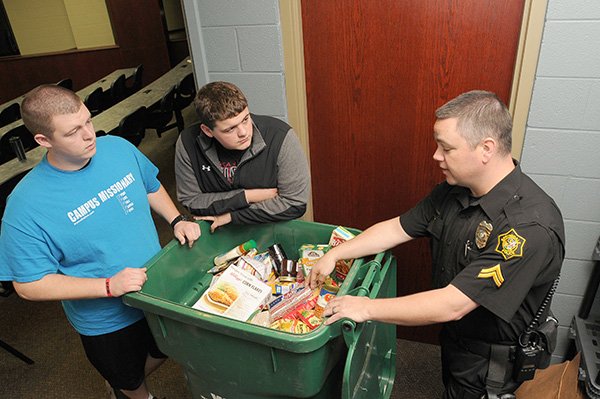 Springdale Har-Ber senior Austin Hazelton, from left, and junior Robert Watson with Cpl. Tommy Wooten look at food donations for the Har-Ber food pantry Thursday, April 25, 2013 at the school in Springdale. The school's groups Safe Wildcat Action Team and Youth for Christ helped start the pantry after some students at the school were unable to have a meal this past Christmas.
