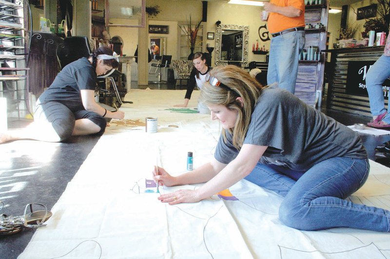 Laurie Howard, front, the owner of Wicked Salon in Sherwood, helps paint a backdrop with Audra Knight, left, and Kathryn Kellogg. All three are members of a team that will participate in the North Pulaski County Relay for Life on May 10 and 11.