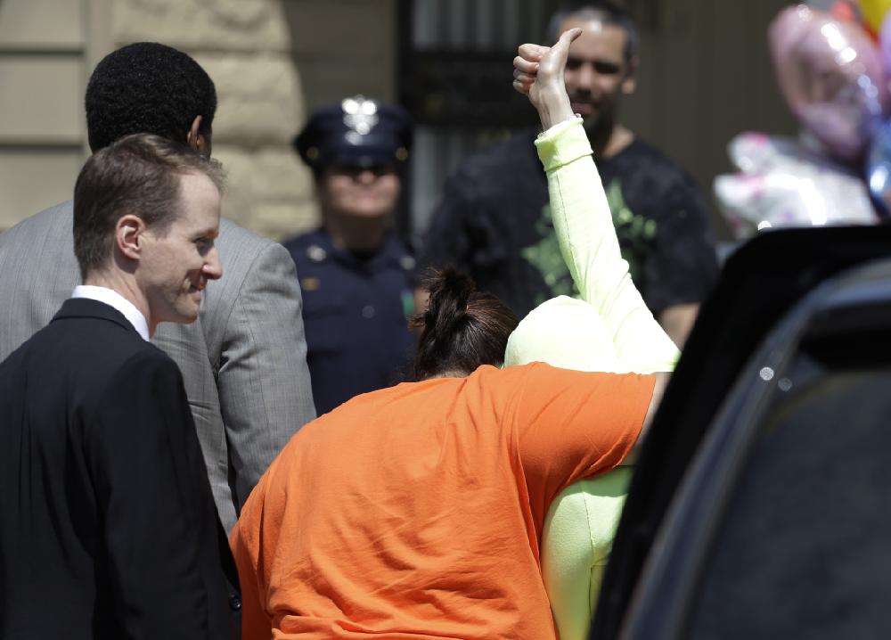 Gina DeJesus gives a thumbs-up as she is escorted toward her home Wednesday, May 8, 2013, in Cleveland. The three women held captive for about a decade at a run-down Cleveland house were apparently bound with ropes and chains, police said Wednesday, while charges were expected by the end of the day against the three brothers under arrest. (AP Photo/Tony Dejak)