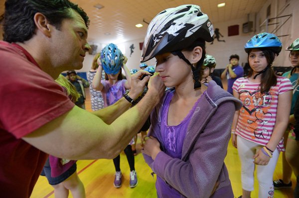 Penn Wilder, left, of Bell Sports helps Sophia Rodriguez, 11, fit into her bicycle helmet Wednesday at Ardis Ann Middle School in Bentonville. Bell Sports, in a partnership with Safe Kids Worldwide and Mercy Health System, donated 650 helmets to students at the school on National Bike to School Day. 