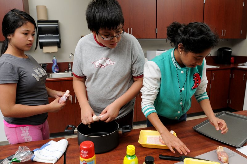 Students from Sonora Middle School, from left, Anahi Arroyo, 12, Christian Beltran, 12, and Xitlalhy Gomez, 13, skin chicken Wednesday in the Cooking Matters after school program at the school in Springdale. 