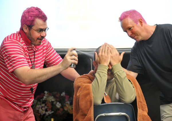 Holt Middle School teacher Brandon Craft (left) and assistant principal Rich Guthrie (right) spray pink hair dye onto the head of their fellow teacher Blaine Sanders Wednesday morning during a morning assembly in Fayetteville. The teachers dyed their hair in an effort to help motivate their students who closed out a year of studying community giving/service. The students efforts resulted in $1,500 being raised to donate to Oliviaâ€™s Basket.