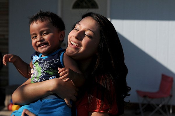 Leslie Silva, 18, laughs as she carries her son, Noah Mauricio, 18 months, outside her home in Springdale. Silva was 16 when Noah was born and went through many challenges, but is getting As and Bs and ready to graduate from Har-Ber High School and hopes to attend the University of the Arkansas. 