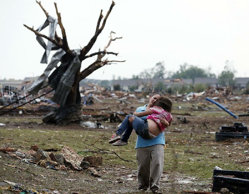 A woman carries her child through a field near the collapsed Plaza Towers Elementary School in Moore, Okla., Monday, May 20, 2013. A tornado as much as a mile (1.6 kilometers) wide with winds up to 200 mph (320 kph) roared through the Oklahoma City suburbs Monday, flattening entire neighborhoods, setting buildings on fire and landing a direct blow on an elementary school. (AP Photo Sue Ogrocki)