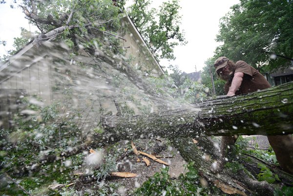 Bill Martin of Professional Tree Service uses a chain saw Tuesday to cut up a tree blown across an alley during Monday’s severe thunderstorms and on the garage of a home on Southeast Third Street near downtown Bentonville. Company owner Chad Williams said the job was the fifth his crew worked on Tuesday. 