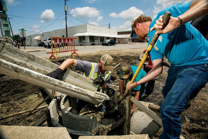 Josh Elliott of Mallard Ready Mix, left, helps Tommy Fowlkes, assistant director of the Conway Street Department, center, and Travis Holland of the Street Department pour concrete for a “drop in,” which will help drain water from the street as part of the construction of Rogers Plaza.