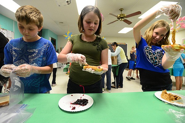Zach McCoy, 11, left, Maeve Smith, 10, and Jacinda Montgomery, 11, work an assembly line Wednesday making peanut butter and jelly sandwiches to go into lunch bags for victims of the Moore, Okla., tornado in their classroom at Bonnie Grimes Elementary School in Rogers. The effort involved four fifth-grade classes, 112 students in all, packing the lunch bags decorated by the students and included hand written notes of support. 