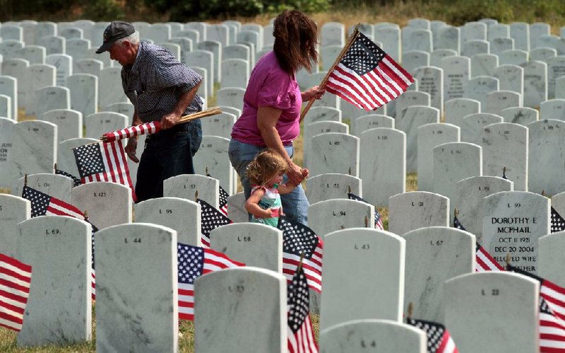 Community volunteers place flags in front of 4,800 headstones last year at the Arkansas State Veterans Cemetery in Sherwood in preparation for Memorial Day ceremonies. 