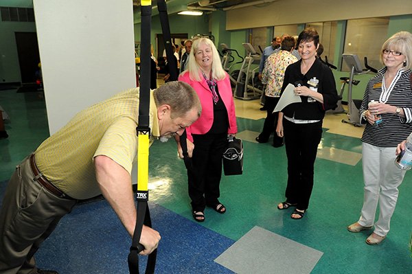 Mike Gilbert, from left, uses workout equipment Thursday as Carolene Thornton, director ChildCare Aware, Barbara Goodman, off campus program manager for NorthWest Arkansas Community College and Kathryn Gough, with U.S. Sen. John Boozman’s office, look on during the opening of the Fitness Center at the Jones Center in Springdale. Several organizations contributed to the center including the Walton Family Foundation, Tyson Foods, Northwest Arkansas Dr Pepper Snapple Group, Walmart/Sam’s Team, and Good Sports. The center features new equipment including 13 pieces of cardiovascular and six strength training machines, dumb bells, mats and flat screen televisions. 
