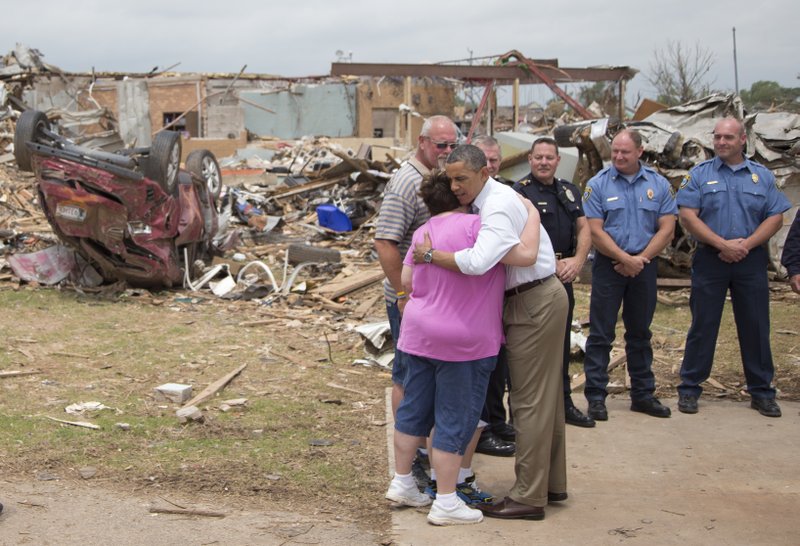 President Barack Obama embraces Julie Lewis, seen with her husband Scott Lewis, and their son Zack, hidden, a third-grader of the destroyed Plaza Towers Elementary School seen in the background, as Obama visits Moore, Okla., Sunday in Moore, Okla., which was utterly devastated by tornadoes and severe weather last week. 
