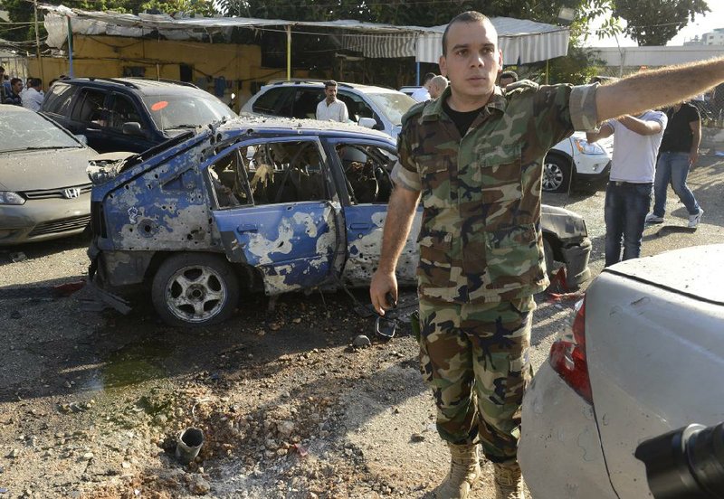A Lebanese army officer stands next to a damaged car as he asks journalists to step back at the scene where a rocket struck a car dealership at the Mar Mikhael district south of Beirut on Sunday. 