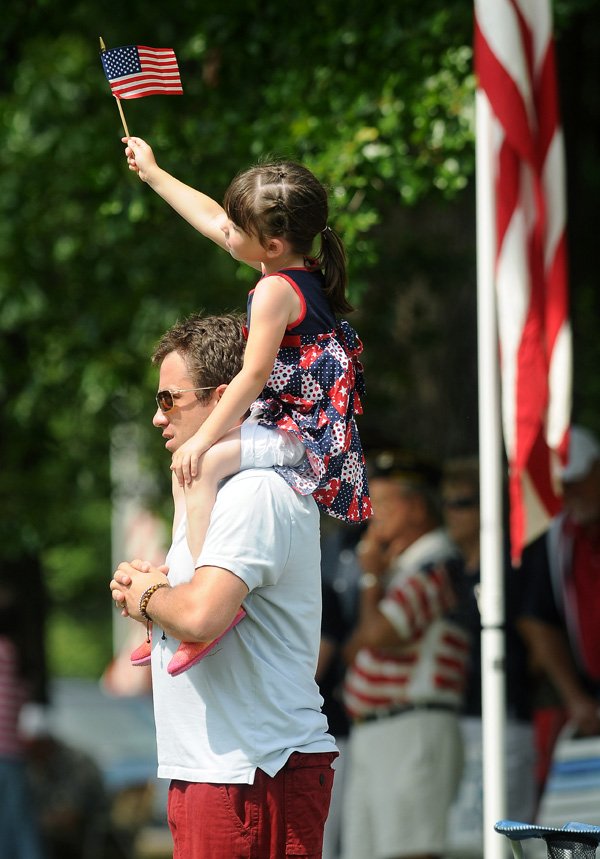 Hannah Hanson, 5, raises the American Flag in the air while sitting atop David Hanson’s shoulders Monday during the annual Memorial Day Service at the Bella Vista Memorial Cemetery. The service included placing of flowers, a roll call of veterans who have died during or after their completed service, and recently commissioned Army officers from the University of Arkansas. 