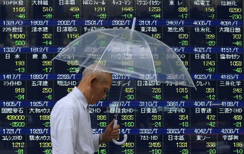 A pedestrian passes a stock board outside a securities firm Thursday in Tokyo. Japan’s Nikkei 225 Stock Average fell again on Thursday, meeting the definition of a correction, a decline of more than 10 percent from a recent peak. 