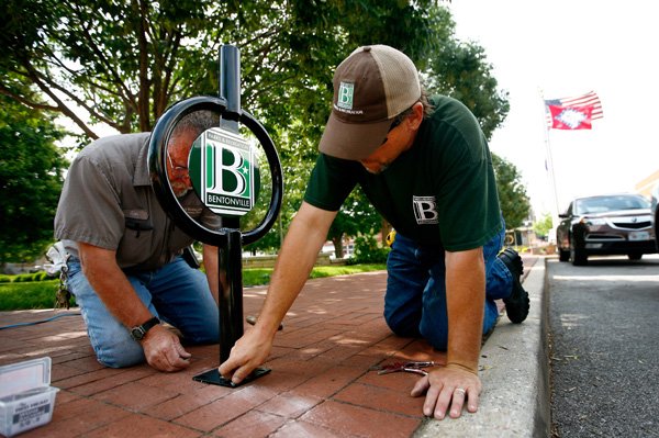 Ken Dawson, left, and Jay Banaszynski, Parks & Recreation employees, install one of six new bicycle racks on Wednesday around the square in downtown Bentonville. Bentonville-based Walmart will hold its annual shareholders meeting Friday at Bud Walton Arena in Fayetteville. 
