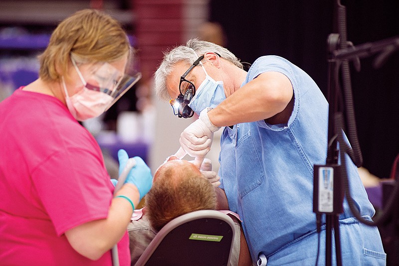 Dr. Lee Hinson, assisted by Karen Trantham, work on a tooth extraction before the patient is fitted for a partial denture during the Arkansas Mission of Mercy two-day free dental clinic sponsored by the Arkansas State Dental Association.