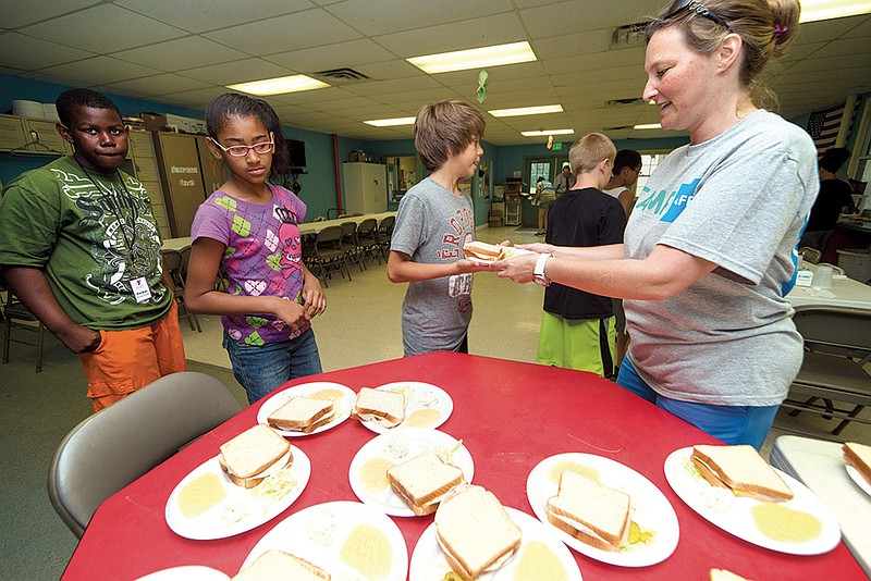 Lynne Chapman, child care director at the YMCA in Hot Springs, hands a lunch plate to Devin Nieto, as Emma Compas and Andrew Starks wait in line. 