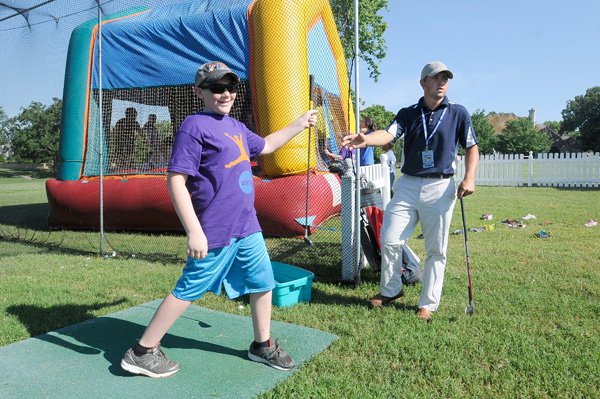 Zecharia Winders, left, is all grins Wednesday after a quick golf lesson at Pinnacle Country Club from Andrew Campisi, right, a coach at First Tee golf learning center. Golf lessons were part of the kids center opening in conjunction with the LPGA golf tournament in Rogers. 