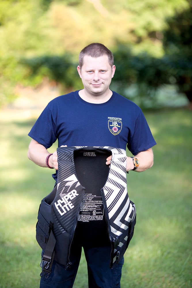 Brian Thomas, 27, of Conway shows the life jacket he wore May 11 when rescuing a man on the Buffalo River during a canoe trip with a group from Central Baptist Church in Conway, where Thomas is a member. The North Little Rock firefighter also helped a woman in the church group who became distressed in the river that day. Thomas said it’s imperative to wear a life jacket, not just have one in the boat.