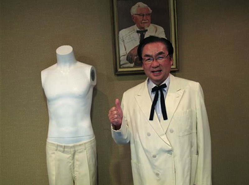 Masao "Charlie" Watanabe, president and chief executive of Kentucky Fried Chicken Japan, stands beneath a portrait of company founder "Colonel" Harland Sanders on Saturday, June 22, 2013, at Heritage Auctions in Dallas. Watanabe is wearing Sanders' trademark white suit jacket and black string tie after he purchased them at the auction, which featured other items, including leg irons that restrained abolitionist John Brown.