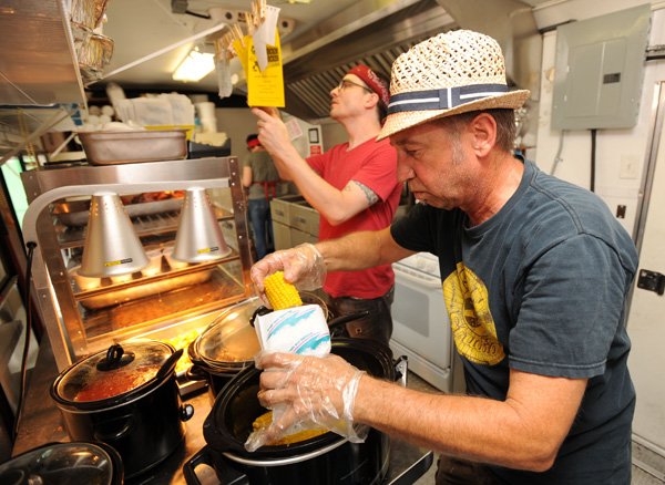 Clayton Scott, right, stand owner, collects corn on the cobb as Matthew Depper, center, and Madison Bliss work to fill orders Friday at Frickin Chicken, a fried-chicken eatery based in a trailer parked near the northeast corner of Rolling Hills Drive and North College Avenue in Fayetteville. 