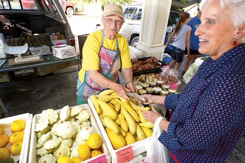 Jean Hughes, left, hands some change to Ann McMillion, who is buying some yellow squash from Hughes at the Arkadelphia Farmers Market.