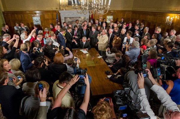 Gov. Mike Beebe is surrounded in April by lawmakers, the media and others as he signs bills related to the expansion of Medicaid funding through the “private option” worked out with the state Legislature