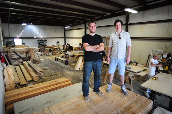 James Smith, right and James Eldridge stand on a load of lumber Tuesday that had just been delivered to their small furniture company in Springdale. James + James Fine Furniture has grown in the last two years. Starting with just the two of them in a garage in Rogers, the business has expanded to a 7,200-square-foot workspace.