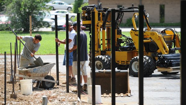 Kyle Langston, left, mixes concrete Wednesday as his uncle, Don Langston, center, and father, Steve Langston, all of Accent Fence in Springdale install a fence surrounding a new recycling drop-off center on North Street between Leverett and Gregg avenues in Fayetteville. 
