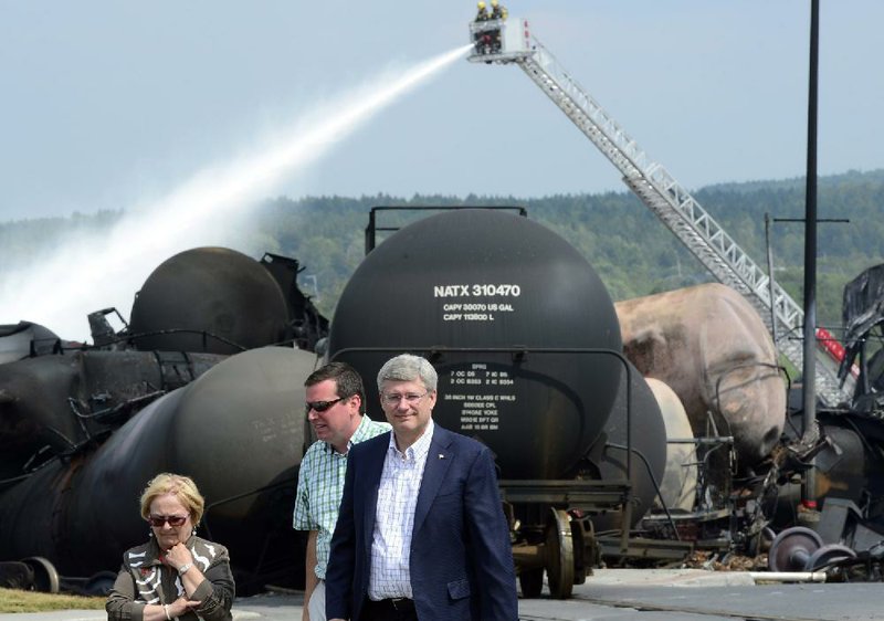 Canadian Prime Minister Harper, right, surveys the scene Sunday, July 7, 2013, in Lac Megantic, Quebec, as firefighters continue to spray derailed tanker cars.  A runaway train derailed Saturday causing explosions of railway cars carrying crude oil and destroyed part of the downtown area of Lac Megantic.   (AP Photo/THE CANADIAN PRESS, Paul Chiasson)