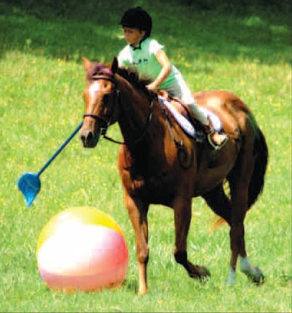 Alyx Swope-Bell, riding sugar, takes a swing at the giant beach ball using a broom as a polo mallet. All eight riders of the Legends class took turns moving the ball across the playing fi eld towards goals at the end. 