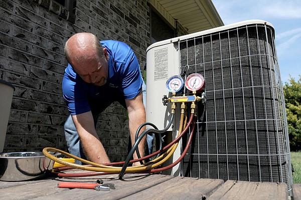 Charles Smith with Heating & Air Solutions hooks up to test the coolant line pressure on a condenser unit Thursday at a home in Springdale. Proper refrigerant pressure is essential for a central air system to work properly. Smith has several easy tips to prolong the life of an air conditioner until including keeping grass and shrubs at least three feet away from the outside unit and when mowing, to always mow away from the unit to keep the mower from blowing clippings into the unit. 